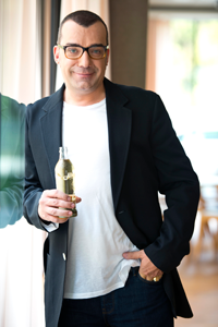 Foto von Thomas Klein lehnend an einer Wand mit einer Getränkeflasche in der Hand.